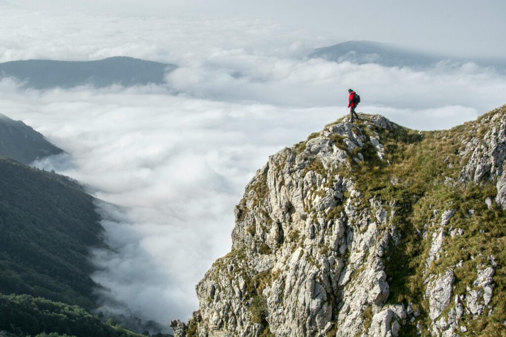 Man standing on top of mountain overlooking cloudy peaks