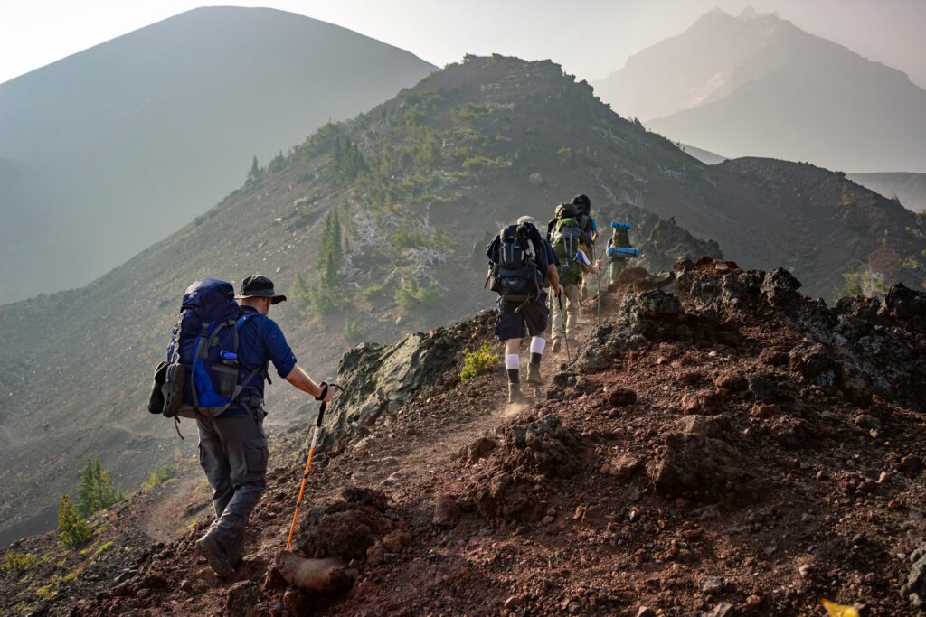 Multiple people hiking a trail along a ridgeline. All have large hiking packs and walking poles